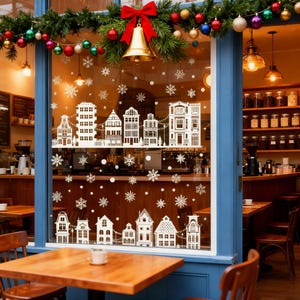 Può includere: Una vetrina di un bar decorata per Natale con ritagli di case bianche e fiocchi di neve. Una ghirlanda di verde, ornamenti e un fiocco rosso con una campana d'oro sono appesi sopra. L'interno presenta tavoli e scaffali con barattoli.