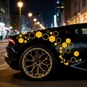 May include: Black sports car with gold rims and yellow hexagon decals. The car is parked on a city street at night, with streetlights illuminating the scene. The decals are of varying sizes.