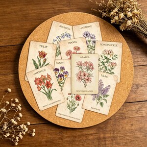 Op de afbeelding: Een verzameling vintage botanische kaarten met verschillende bloemen zoals tulpen, azalea's en seringen. Elke kaart toont een gedetailleerde illustratie van de bloem met de naam en een korte zin. De kaarten zijn gerangschikt op een ronde kurken plank.
