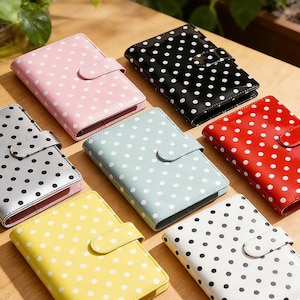 Op de afbeelding: Een verzameling kleurrijke notitieboekjes met witte stippen. De notitieboekjes zijn verkrijgbaar in verschillende kleuren, waaronder roze, zwart, zilver, lichtblauw, rood, geel en wit. Elk notitieboekje heeft een bijpassende sluiting.