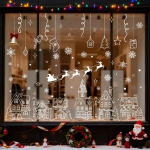 Peut inclure: Une vitrine de Noël avec des silhouettes blanches d'un village, de flocons de neige, du traîneau du Père Noël et de décorations suspendues. La vitrine comprend une cloche, un sucre d'orge, une chaussette, une maison, un arbre, une étoile et un cadeau. Des lumières colorées et des décorations festives complètent la scène.