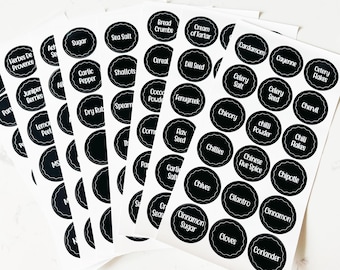 May include: A set of black and white round spice jar labels with various spice names printed in white. The labels are arranged in rows and columns on a white surface.