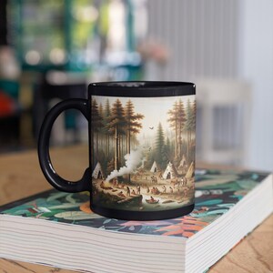 May include: Black coffee mug featuring a detailed landscape scene of a forest with teepees, people, and a river. The mug has a black handle and rim. The mug is sitting on a book with a colorful floral design.