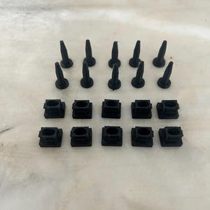 Puede incluir: Un conjunto de chinchetas y bases cuadradas de plástico negro. Las chinchetas tienen una punta puntiaguda y las bases tienen un pequeño agujero en el centro.