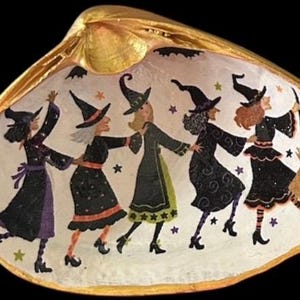 May include: A painted seashell featuring five witches in black dresses and pointed hats, dancing in a circle. The shell has a gold rim and a white interior with stars and bats. A whimsical Halloween decoration.