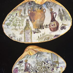 May include: Two gold-painted seashells with a white background and a painted design of olive branches, bottles, and a jar. The design is reminiscent of an Italian countryside.