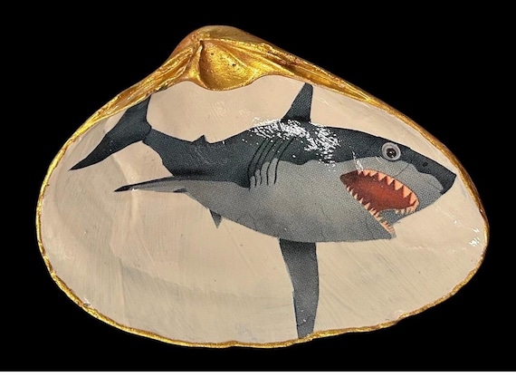 A real clam shell decoupaged with a grinning googly-eyed shark — genuinely weird, one-of-a-kind coastal kitsch that you'd never find in a store.