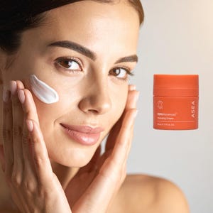 May include: A woman applying white hydrating cream to her face. An orange jar of RENUAdvanced Hydrating Cream is visible. The jar has white text and a logo. The cream is 1.7 fl oz.
