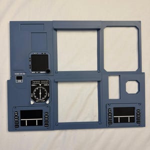 May include: A blue aircraft cockpit instrument panel replica featuring various rectangular cutouts, a circular navigation gauge with DME-L and DME-R labels, and small control displays with buttons labeled BRT, DIM, MSG, and POS.