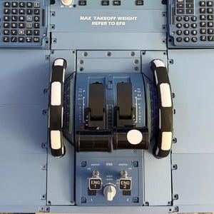 Pode incluir: Um quadrante de aceleração de aeronave azul-claro com duas alavancas de motor pretas, dois punhos curvos com detalhes brancos e dois teclados alfanuméricos. O painel exibe o texto MAX TAKEOFF WEIGHT REFER TO EFB, ENG 1 e ENG 2.