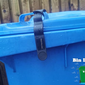 Puede incluir: Una cerradura de contenedor negra con el texto "Bin Locks" y una ilustración de dibujos animados de un contenedor verde con una cara. La cerradura del contenedor está unida a un contenedor de reciclaje azul.