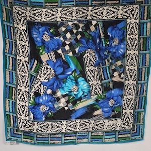 May include: A square silk scarf featuring a vibrant floral pattern with large blue and turquoise flowers on a black background. The design includes a decorative white and black border with geometric motifs and a striped outer edge in blue and green.
