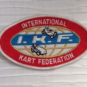 May include: Oval patch with red border and white stitching. The patch features the text "INTERNATIONAL KART FEDERATION" in red and white. The center has a blue and gold design with the letters "I.K.F." and images of a kart and driver.