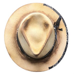 Può includere: Cappello fedora beige dall'aspetto invecchiato. Presenta una fascia nera con perline bianche e un bordo con motivo paisley bianco e nero. Un nastro nero è legato attorno al cappello, di circa 30 cm di diametro.