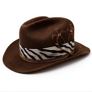 Op de afbeelding: Bruine fedora hoed met een brede rand. De hoed heeft een zebra gestreepte band en geborduurde palmboomontwerpen. Een dun koord omwikkelt de basis van de kroon. Een stijlvol accessoire.