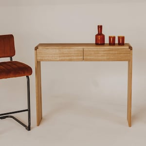 May include: A brown velvet bar stool with a black metal frame sits next to a wooden console table with two drawers. The table has a brown finish and is decorated with three amber glass bottles.