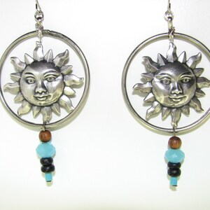 May include: Silver hoop earrings with a sun face charm and blue and brown beads hanging from the bottom.