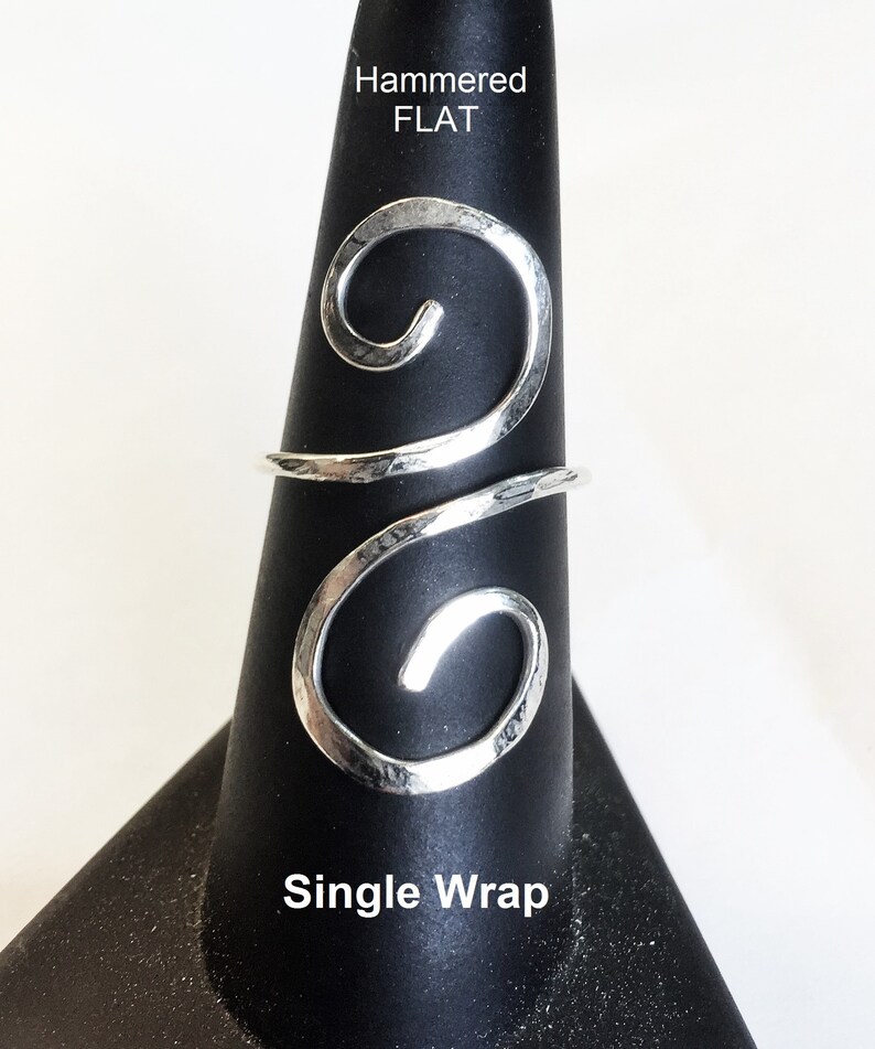 May include: A silver hammered flat ring with a single wrap design. The ring is on a black ring display stand. The text "Hammered FLAT" and "Single Wrap" is visible on the stand.