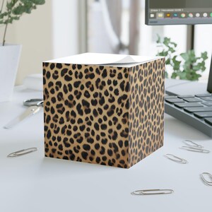 May include: A brown and black leopard print sticky note holder. The holder is cube shaped and has a white top.
