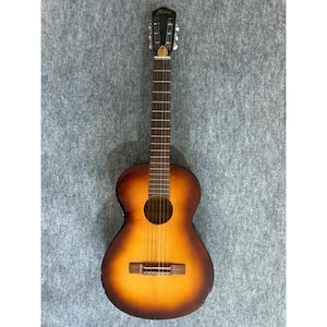 May include: A sunburst acoustic guitar with a dark brown to light amber gradient finish on the body. The instrument features a black headstock with the brand name Harmony in gold lettering, a dark fretboard, six strings, and a wooden bridge.