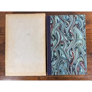 May include: A rectangular book with a plain, light beige cover positioned next to a book featuring a dark purple spine and a front cover decorated with a swirling, marbled pattern in shades of teal, black, and deep red, creating a distinct contrast.