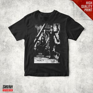 Puede incluir: Una camiseta negra de manga corta con un estampado gráfico blanco de dos figuras en un entorno oscuro y texturizado. El texto "THE SISTERS OF MERCY" está impreso en blanco debajo de las figuras. La prenda tiene cuello redondo y corte estándar.