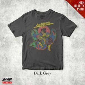 May include: A dark grey short-sleeve t-shirt featuring a graphic print of a warrior figure with a dragon-like creature. The text Dokken appears at the top in yellow, and the text Beast From The East is printed in red within the central illustration.