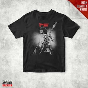 May include: Black t-shirt featuring a grayscale image of a musician playing a bass guitar. The band name "Thin Lizzy" is printed in red above the image. The words "HIGH QUALITY PRINT" are in a red box in the upper right corner.