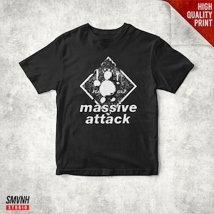 Puede incluir: Camiseta negra con un diseño gráfico blanco. El diseño incluye una forma de diamante con una figura estilizada y las palabras "massive attack". La camiseta tiene mangas cortas y cuello redondo. El texto "High Quality Print" también es visible.