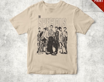 May include: A beige short-sleeve t-shirt featuring a black and white graphic print of the band The Specials. The design includes the text THE SPECIALS in a bold, outlined font above a group portrait of the seven band members in formal attire.