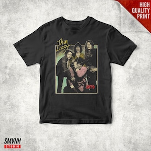 May include: Black t-shirt featuring a vintage graphic of the band Thin Lizzy with the year 1979. The graphic is in a rectangular frame with the band's name in a stylized font. The shirt is on a white surface.