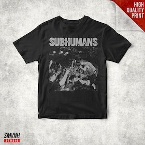 May include: A black short-sleeved t-shirt featuring a white graphic print of a live concert scene. The text SUBHUMANS is printed in a bold, distressed white font above the image, which depicts a performer on stage and a crowd of people.