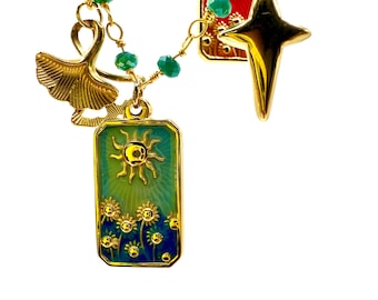 May include: Gold-toned necklace with multiple charms and green beads. Charms include a ginkgo leaf, a four-pointed star, and two rectangular pendants. One pendant features a sun over a field of sunflowers, the other a sunburst on a red background.