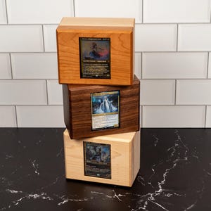 May include: A stack of three rectangular wooden boxes, each featuring a clear front window displaying a collectible trading card. The top box is light brown, the middle box is dark brown, and the bottom box is a pale, natural wood color.