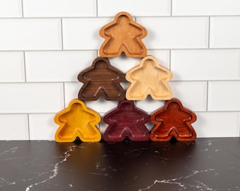 May include: A collection of six wooden game piece trays in various colors, including light brown, dark brown, yellow, purple, and red. The trays are arranged in a pyramid shape against a white tile background.