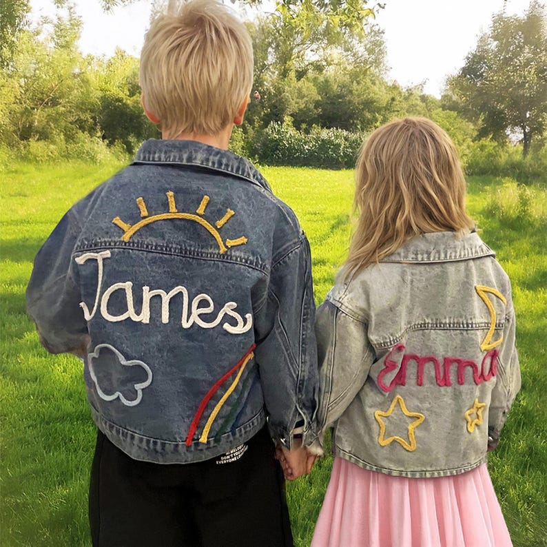 May include: Two denim jackets with embroidered designs. The blue jacket has a yellow sun, rainbow, cloud, and the name "James". The light blue jacket has a pink moon, two yellow stars, and the name "Emma".