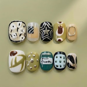 May include: A set of ten artificial nails with various designs. The designs include floral patterns, geometric shapes, a star, and the word "fresh". Colors include white, black, green, and beige.