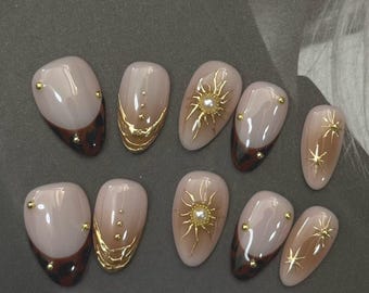 Unghie finte Golden Sun, color tortora e marrone, con dettagli in oro cromato e perla, forma a mandorla corta, fatte a mano, riutilizzabili ed eleganti.