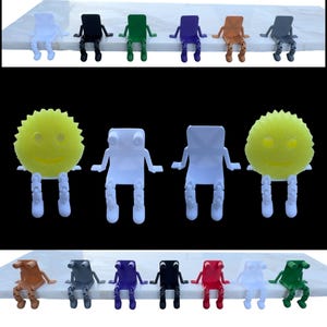 May include: A collection of colorful, small, person-shaped objects. The figures are in various colors, including white, black, green, purple, orange, gray, and red. Some figures have a sponge-like body with a smiling face. The figures are sitting on a white surface.