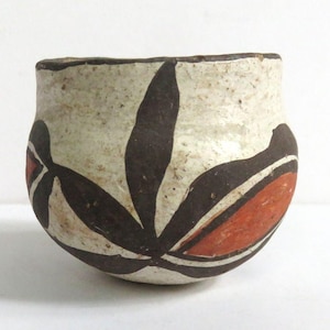 May include: A small, handmade ceramic bowl with a cream-colored exterior. The bowl features a dark brown leaf-like design with red and white accents. The rim is dark brown. The bowl is likely used for decorative purposes.