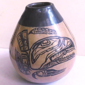 May include: A tan-colored, gourd-shaped vase with a black rim and intricate black tribal art designs. The artwork features stylized animal and geometric patterns, creating a unique decorative piece.
