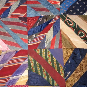May include: Close-up of a patchwork quilt composed of various fabrics, including striped and patterned textiles. The quilt features a geometric design with diagonal lines and a mix of colors like red, blue, and green. The quilt's construction is visible.
