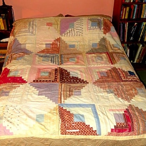 May include: A handmade quilt with a patchwork design, featuring squares of various fabrics in shades of red, pink, blue, and cream. The quilt is spread across a bed, showcasing its intricate patterns and textures. The quilt's design is a log cabin style.