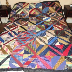 May include: A patchwork quilt made from various patterned fabrics, including stripes and geometric designs. The quilt features a black border and a wide array of colors, including red, blue, green, and brown. The quilt is displayed on a bed.