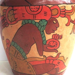 May include: A hand-painted ceramic vase with a detailed illustration. The artwork features a figure in shades of brown, red, and green, with a yellow background. The design appears to be inspired by ancient art.