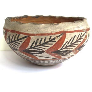 May include: A handmade ceramic bowl with a cream-colored exterior and a wavy rim. The bowl is decorated with a red and black leaf pattern around the sides and a series of thin brown lines near the base. The interior is a warm orange color.