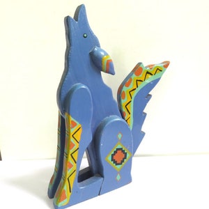 May include: A blue wooden sculpture of a howling wolf with Native American-inspired geometric patterns in orange, yellow, and turquoise. The wolf is painted in a muted blue with a raised head and open mouth.