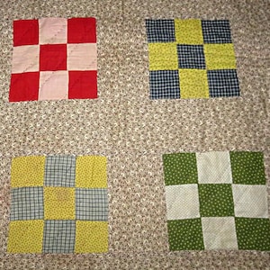 May include: A quilt featuring a beige background with a small brown floral pattern. Four square blocks are appliqued onto the surface, each composed of a nine-patch grid. The blocks feature red, pink, yellow, blue, green, and white fabric squares.