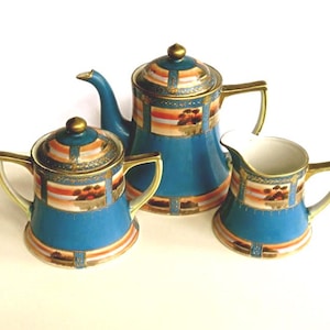 May include: A vintage tea set featuring a teapot, sugar bowl, and creamer. The set is teal with gold trim and decorative panels of orange, brown, and white. The teapot has a lid and a curved spout. The sugar bowl has a lid and two handles. The creamer has a handle.