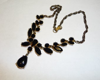 May include: A gold chain necklace with a black teardrop pendant and black gemstone accents.